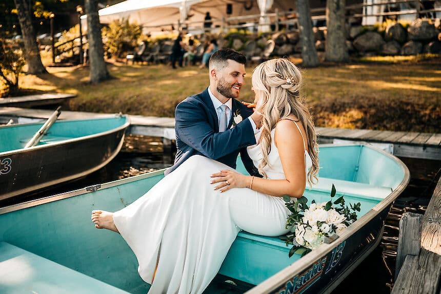 A bride and groom share a tender moment in a small boat, surrounded by a scenic outdoor setting.