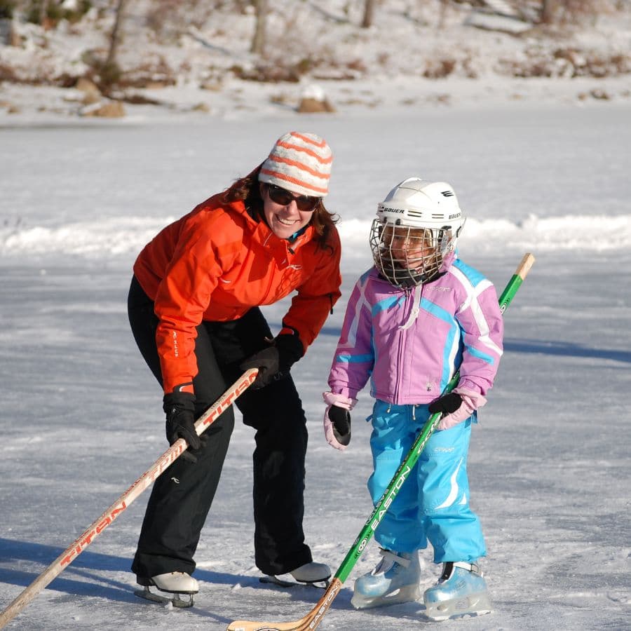 A woman and a girl smile and play hockey on an outdoor ice rink.