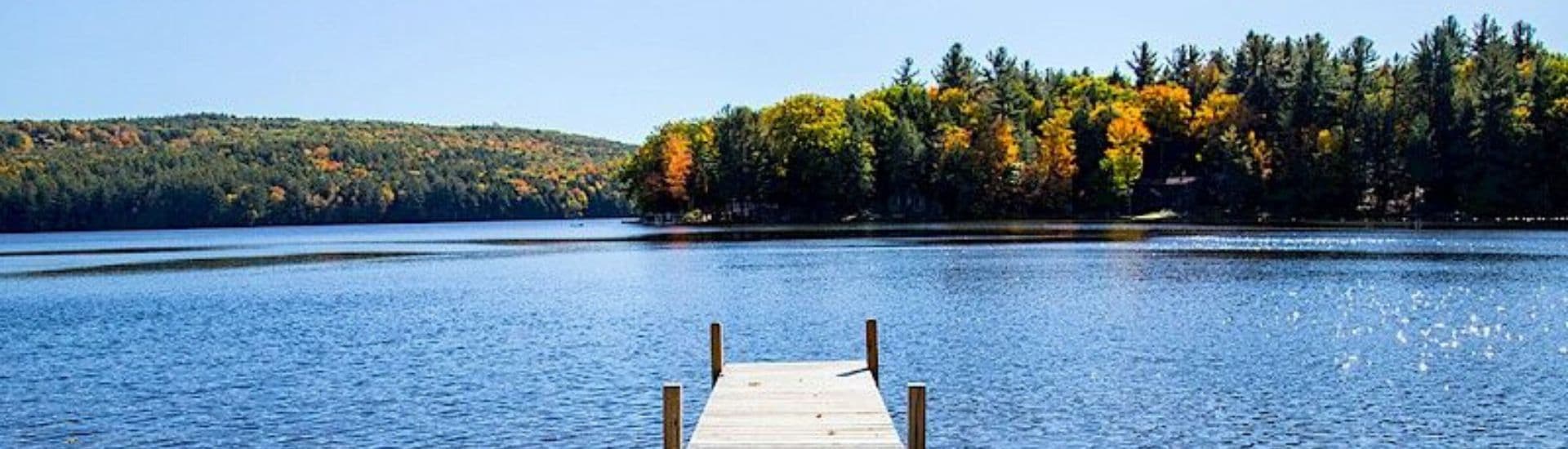 A serene lake view with autumn trees and a wooden dock extending into the water.