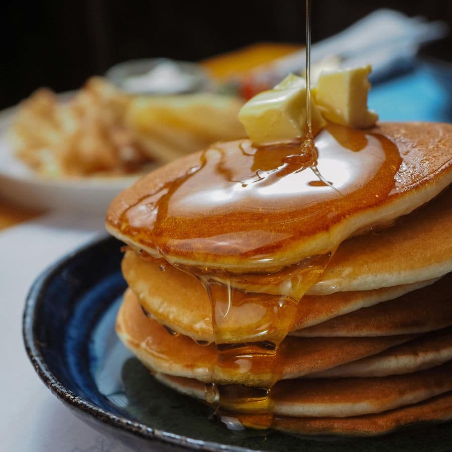A stack of pancakes drizzled with syrup and topped with a pat of butter.