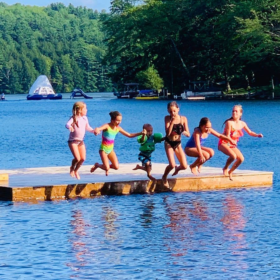 Children jumping off a wooden dock into a lake on a sunny day.
