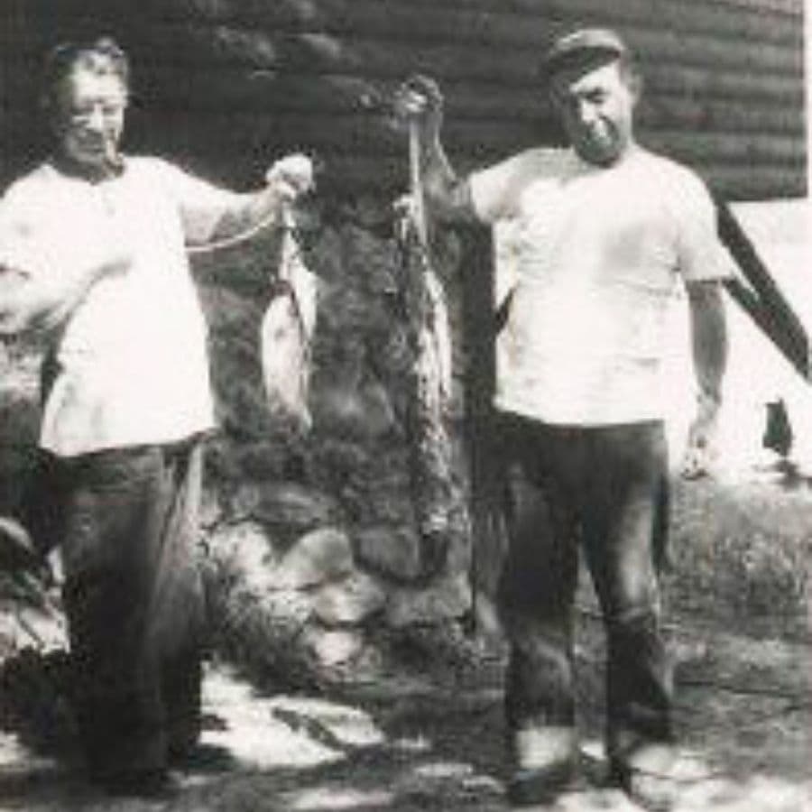Two men holding fish in front of a stone wall.