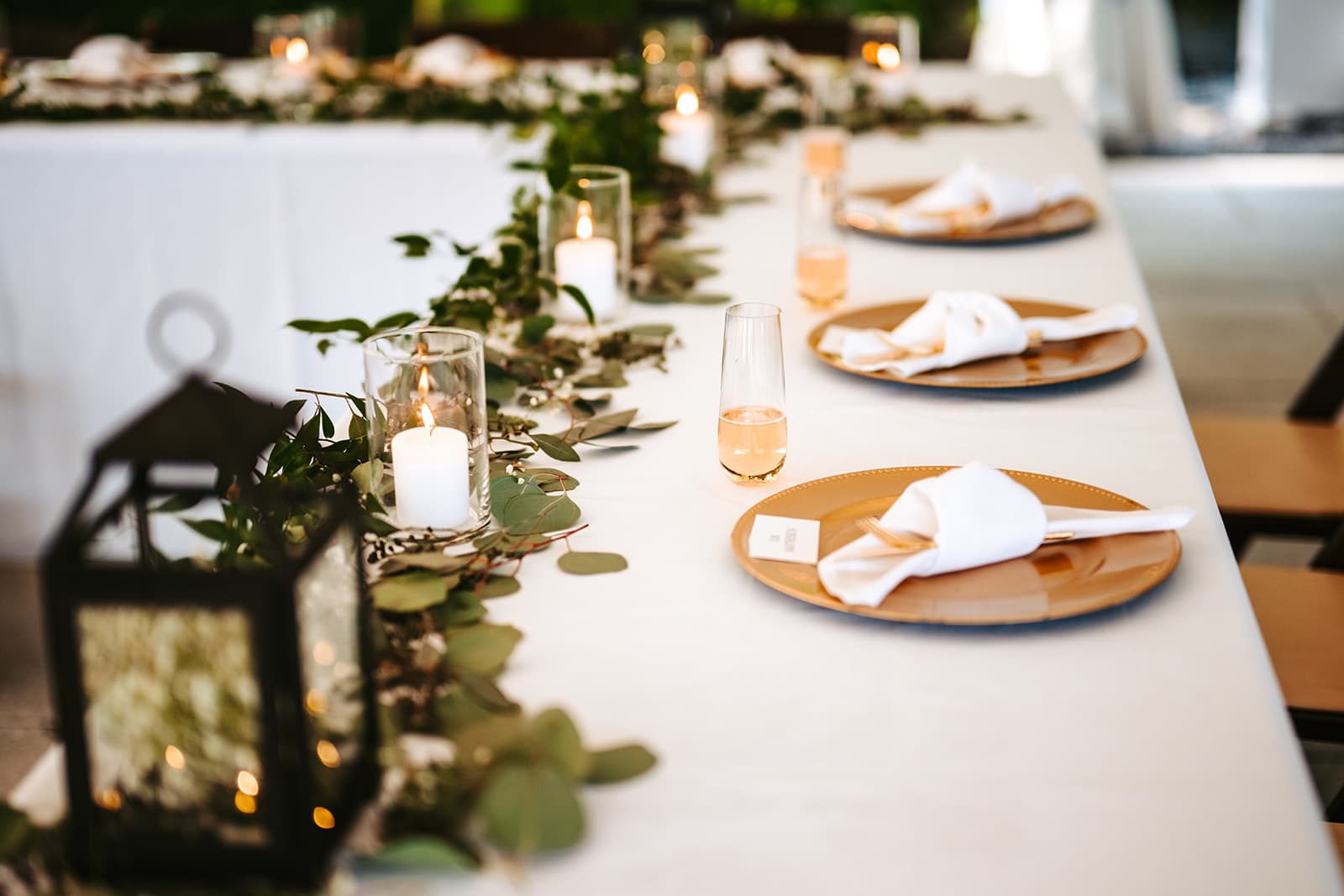 A beautifully set dining table adorned with greenery, candles, and gold plates.