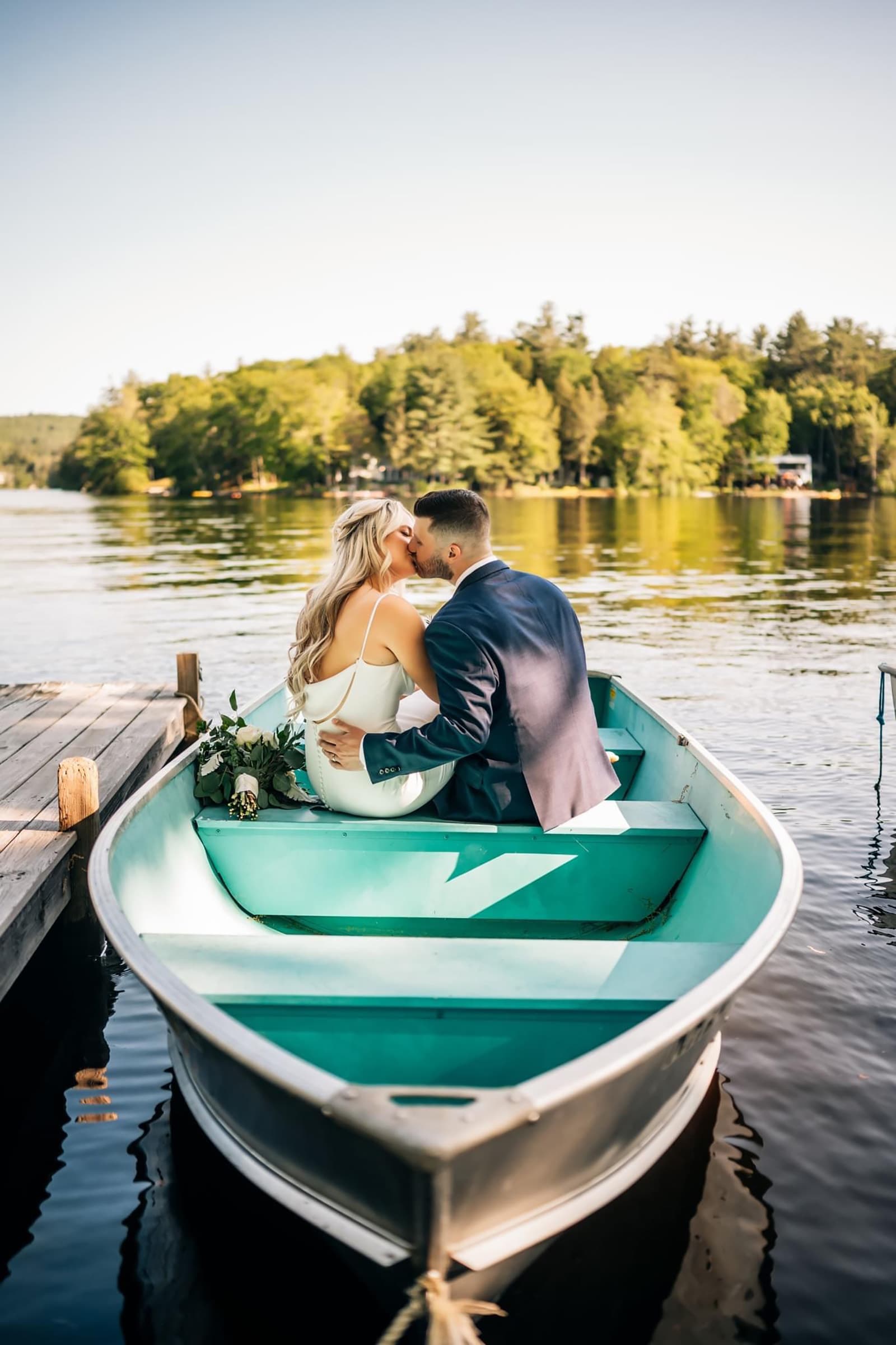 A couple shares a kiss while sitting in a small boat on a serene lake.