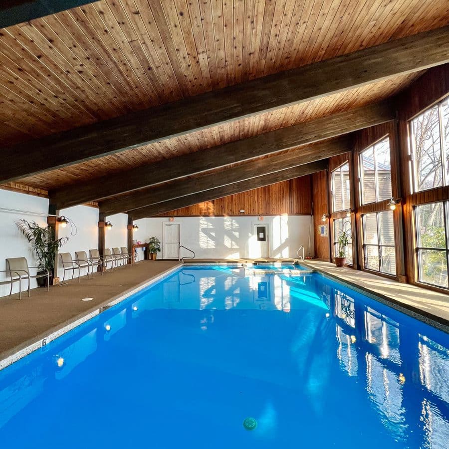 Indoor swimming pool with wooden beams and large windows.