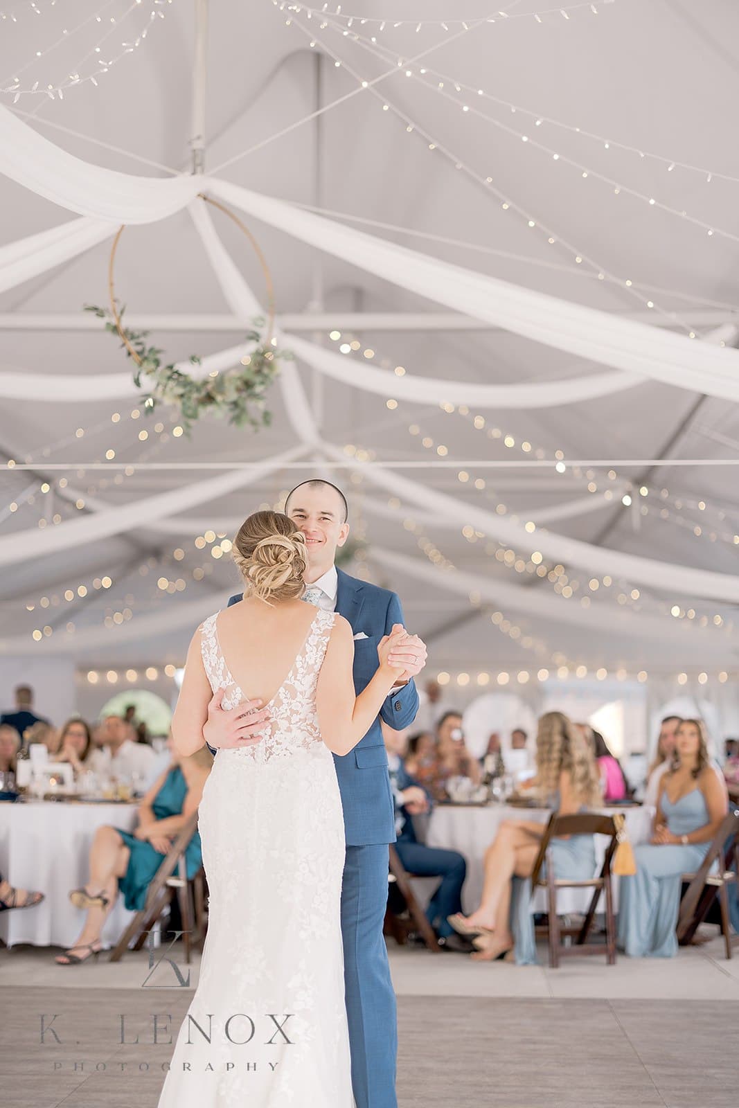 A bride and groom dance together under a beautifully decorated tent filled with guests.