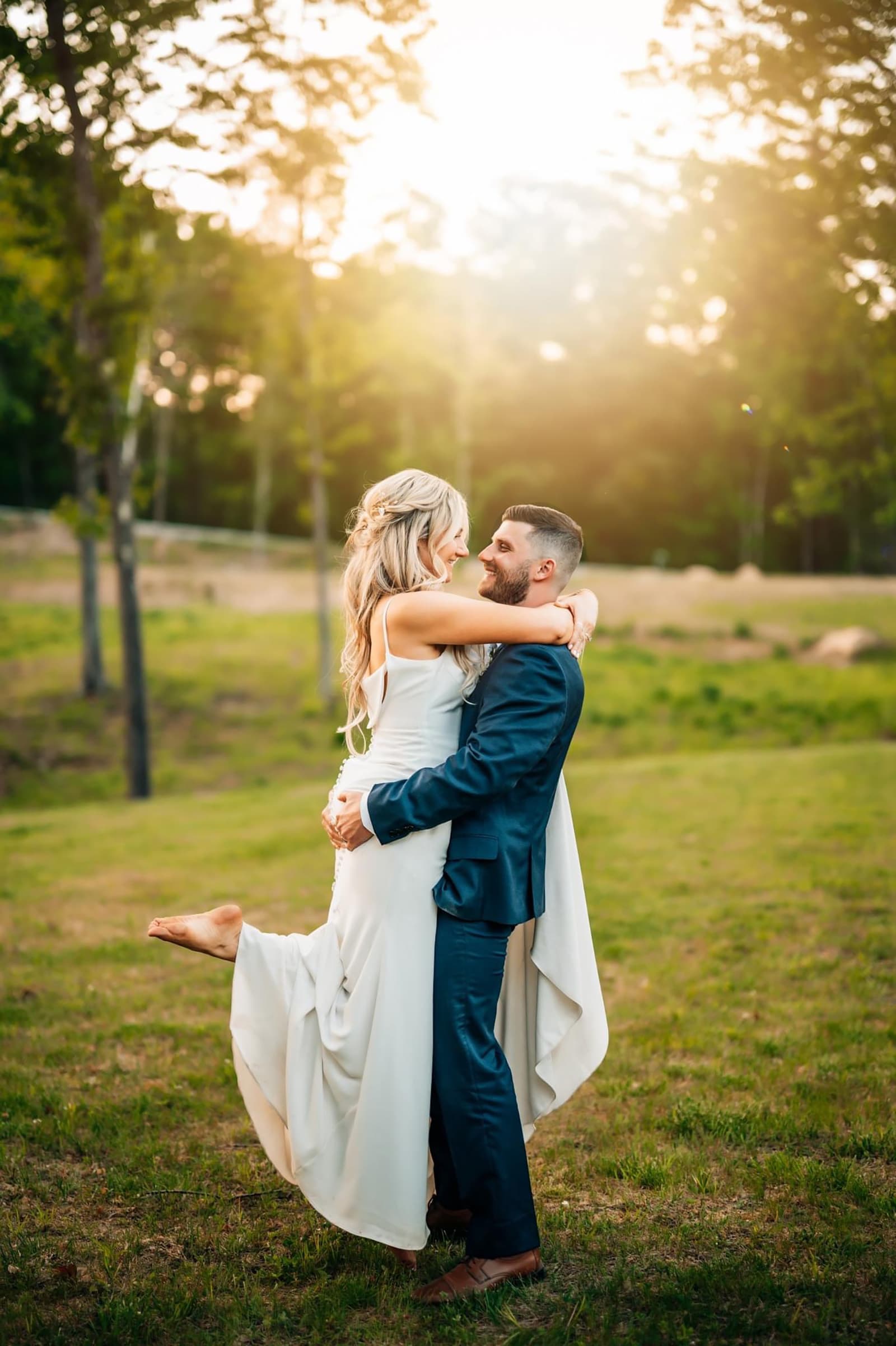 A joyful couple embraces in a sunlit outdoor setting, with the woman lifted off the ground.