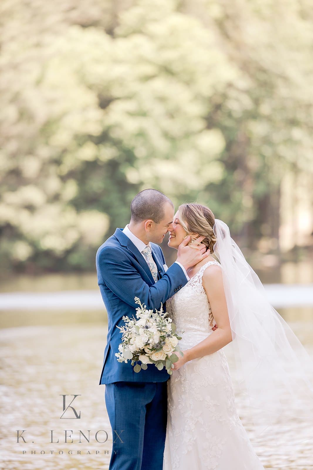 A bride and groom share a joyful kiss by a serene lakeside.