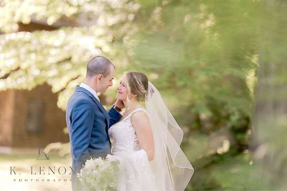 A bride and groom share a tender moment surrounded by greenery on their wedding day.