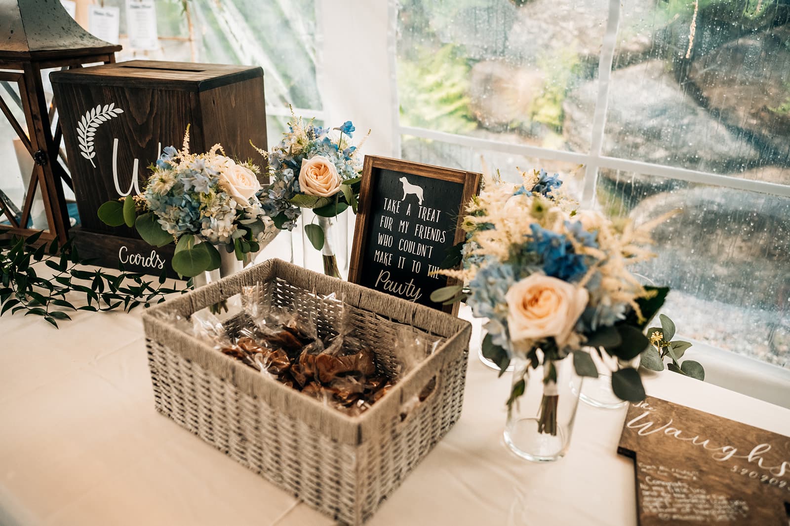 A decorated table at an event featuring floral arrangements, a sign about dog treats, and a card box.
