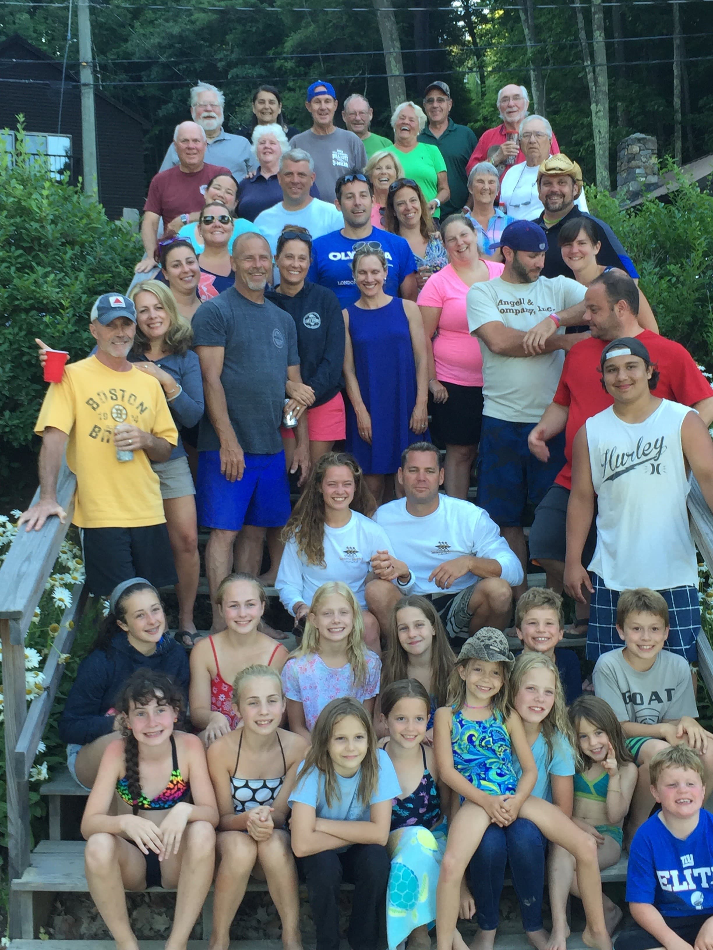 A large group of adults and children poses together on a set of stairs surrounded by greenery.