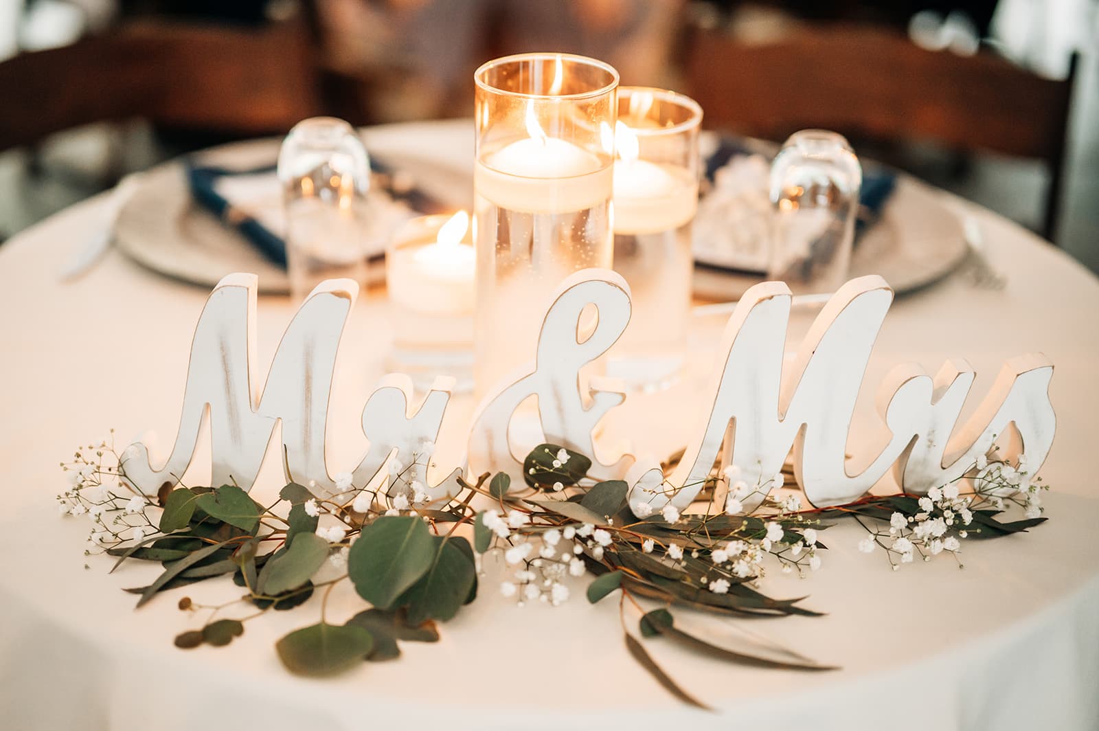 White decorative "Mr & Mrs" lettering surrounded by greenery and candles on a table.