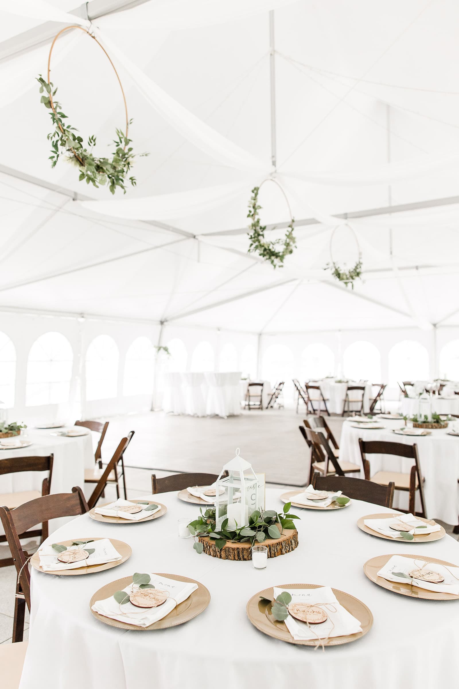 A beautifully decorated dining area in a tent with tables set for an event, featuring greenery and elegant tableware.