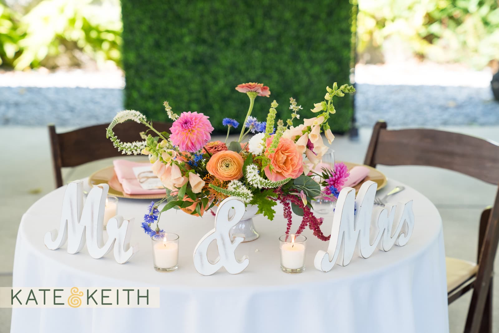 A floral centerpiece on a table with "Mr" and "Mrs" signs and candles, set for a wedding.