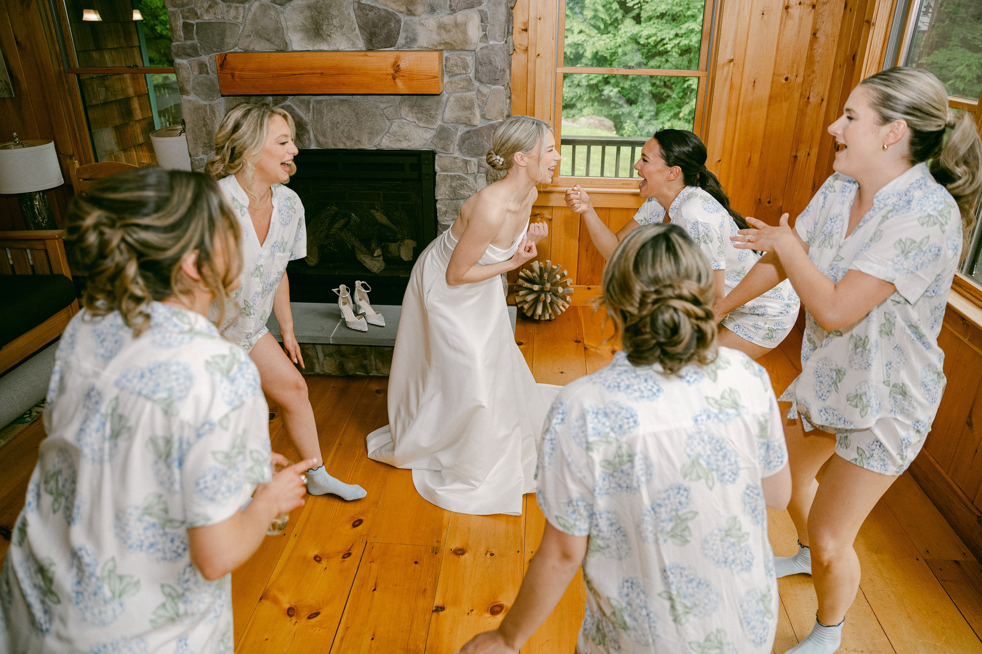 A bride in a white dress laughs and celebrates with her five bridesmaids in matching floral pajamas.