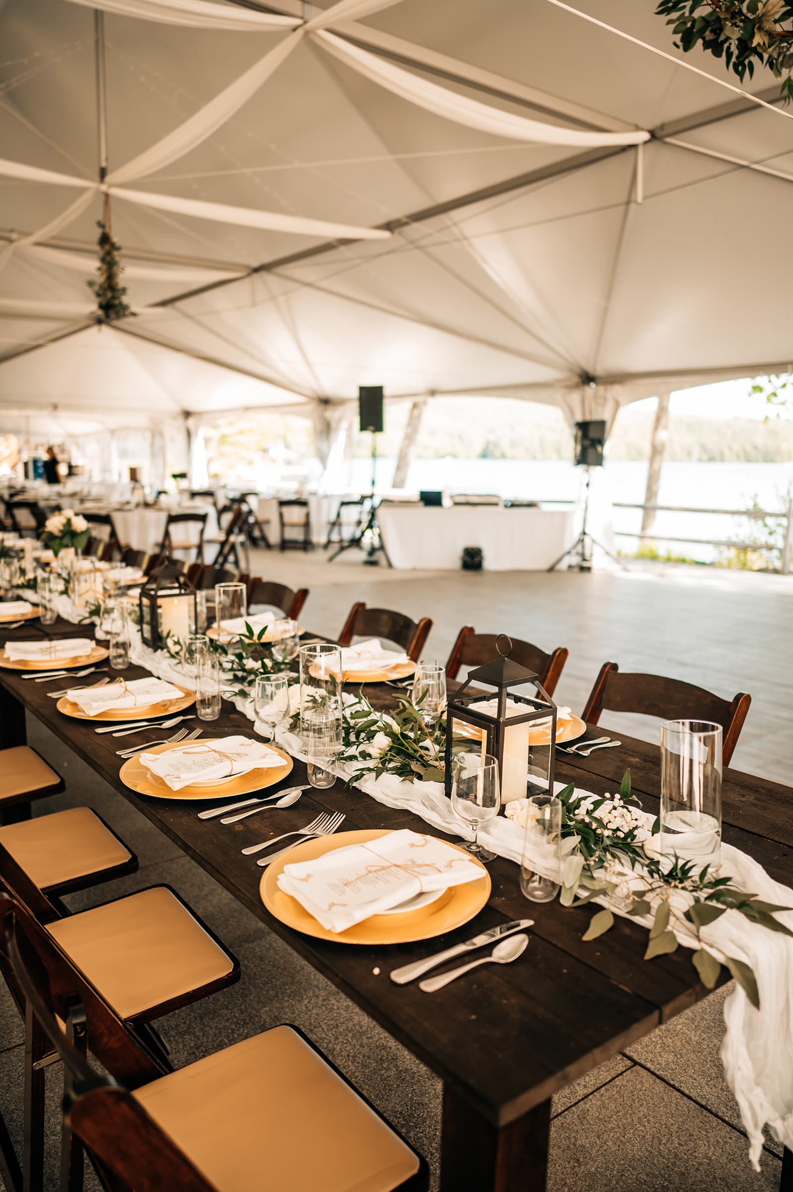 A beautifully arranged banquet table set with gold plates, crystal glasses, and elegant decorations under a large tent.