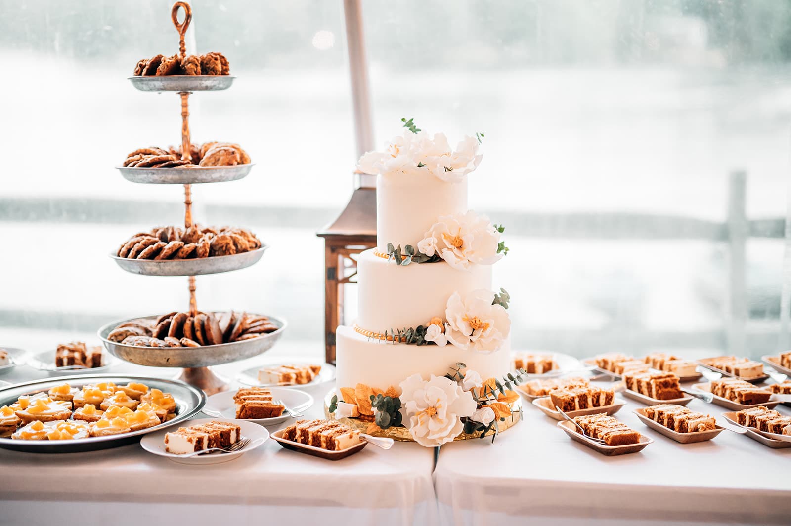 A beautifully decorated three-tiered wedding cake with floral accents, surrounded by assorted desserts on a table.