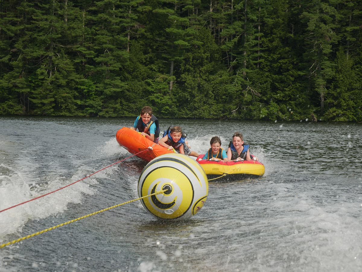 Four kids enjoy tubing on a lake, laughing as they are pulled by a boat.
