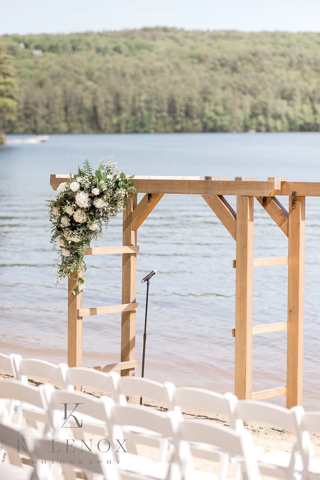 A floral-decorated wooden arch is set up by a serene lakeside for a wedding ceremony.