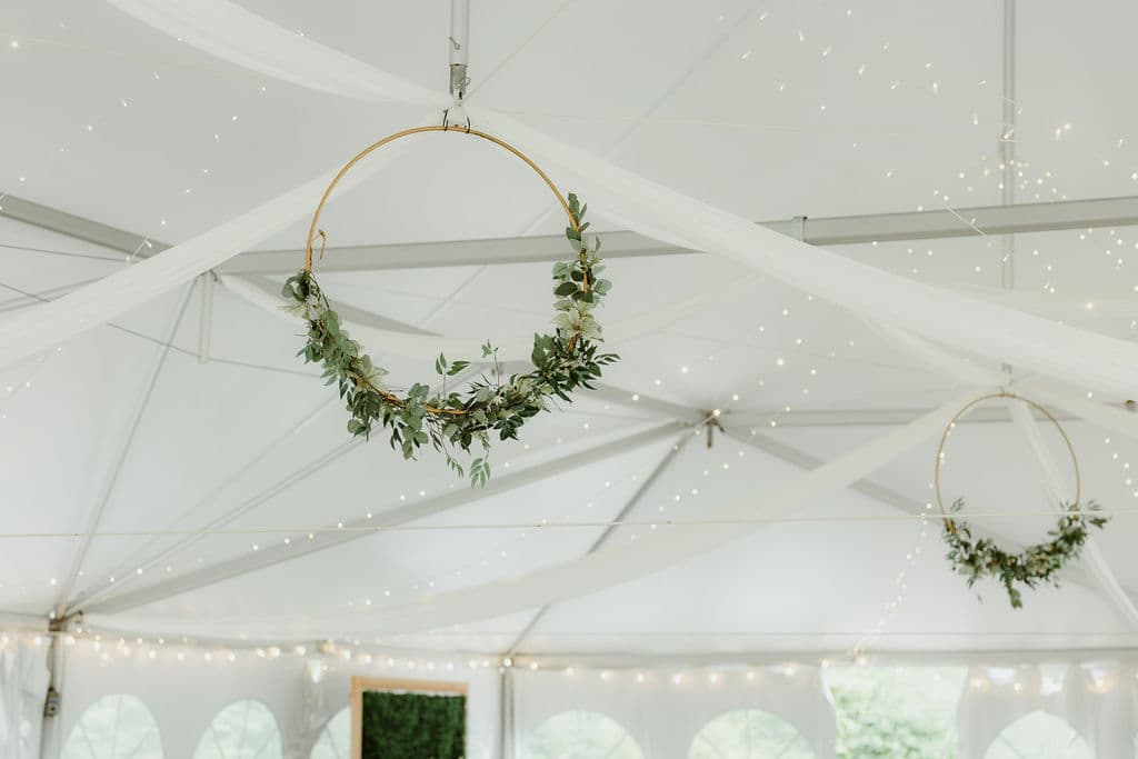 Decorative greenery hangs from circular frames in a tent adorned with soft lighting.