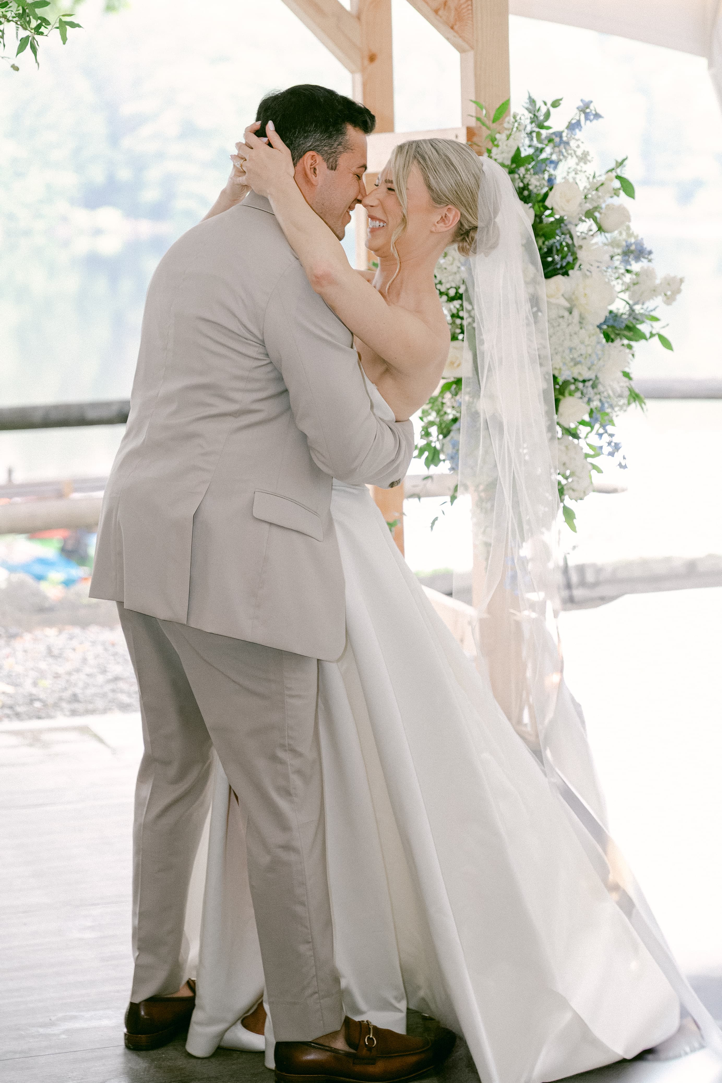 A bride and groom embrace joyfully under a decorative arch at their wedding ceremony.