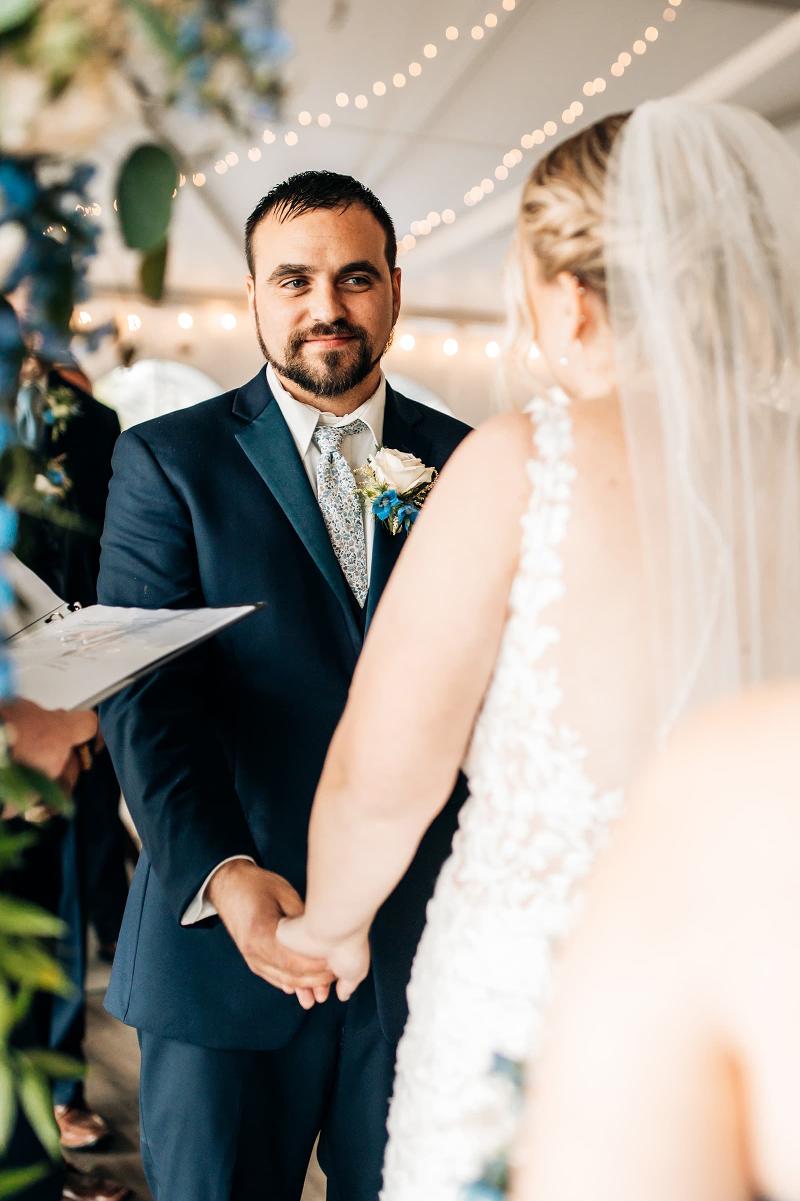 A bride and groom hold hands during their wedding ceremony under soft lighting.