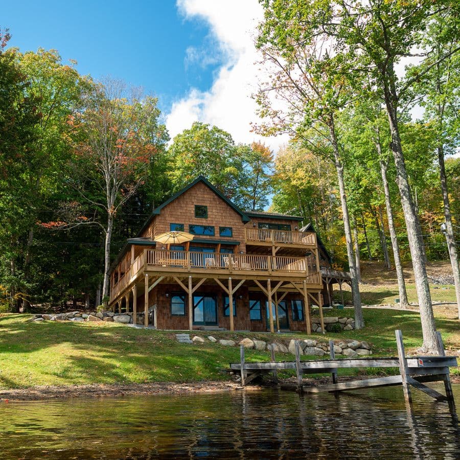 A lakeside cabin with wooden balconies surrounded by colorful autumn trees.