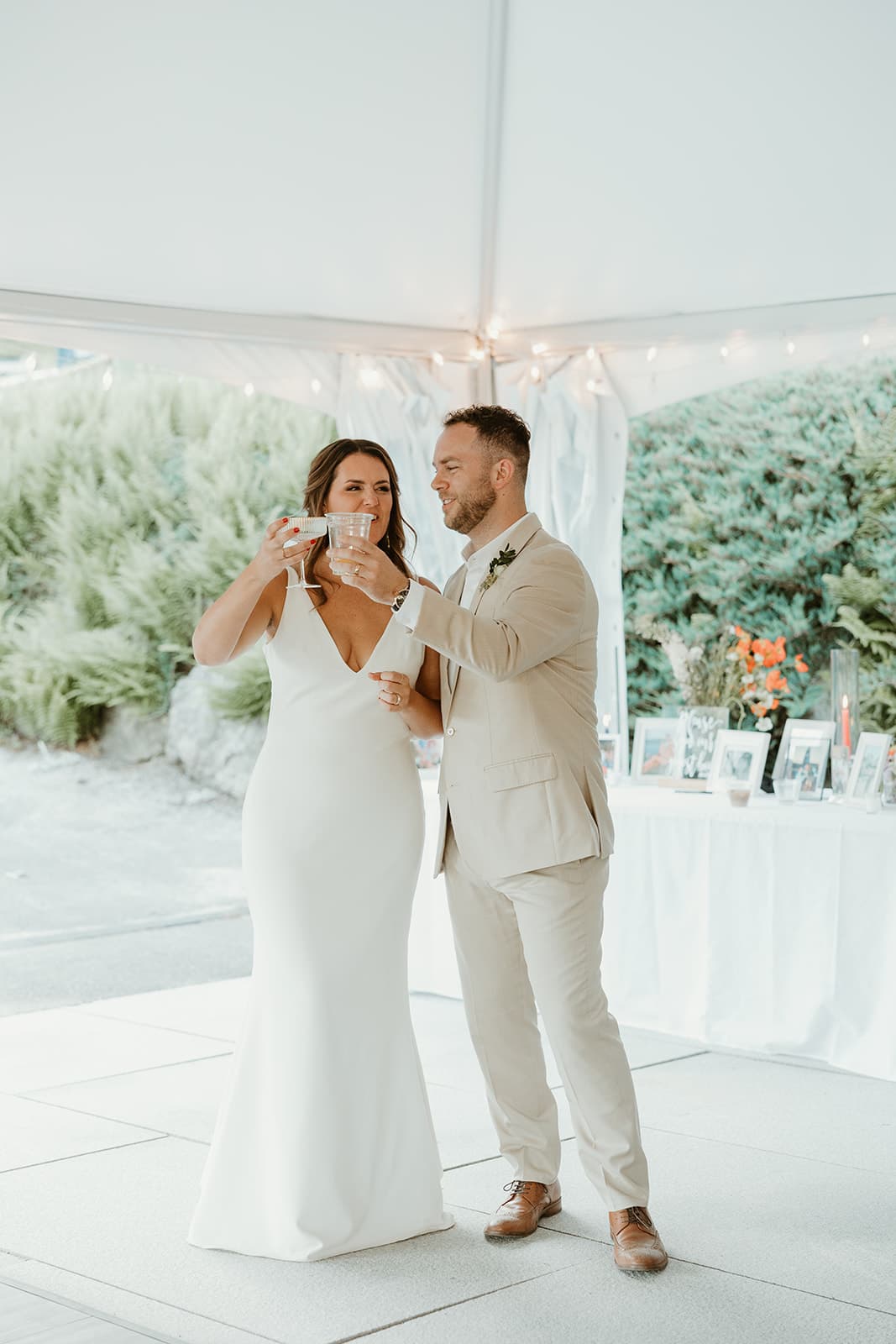 A bride and groom toast at their wedding reception under a tent.