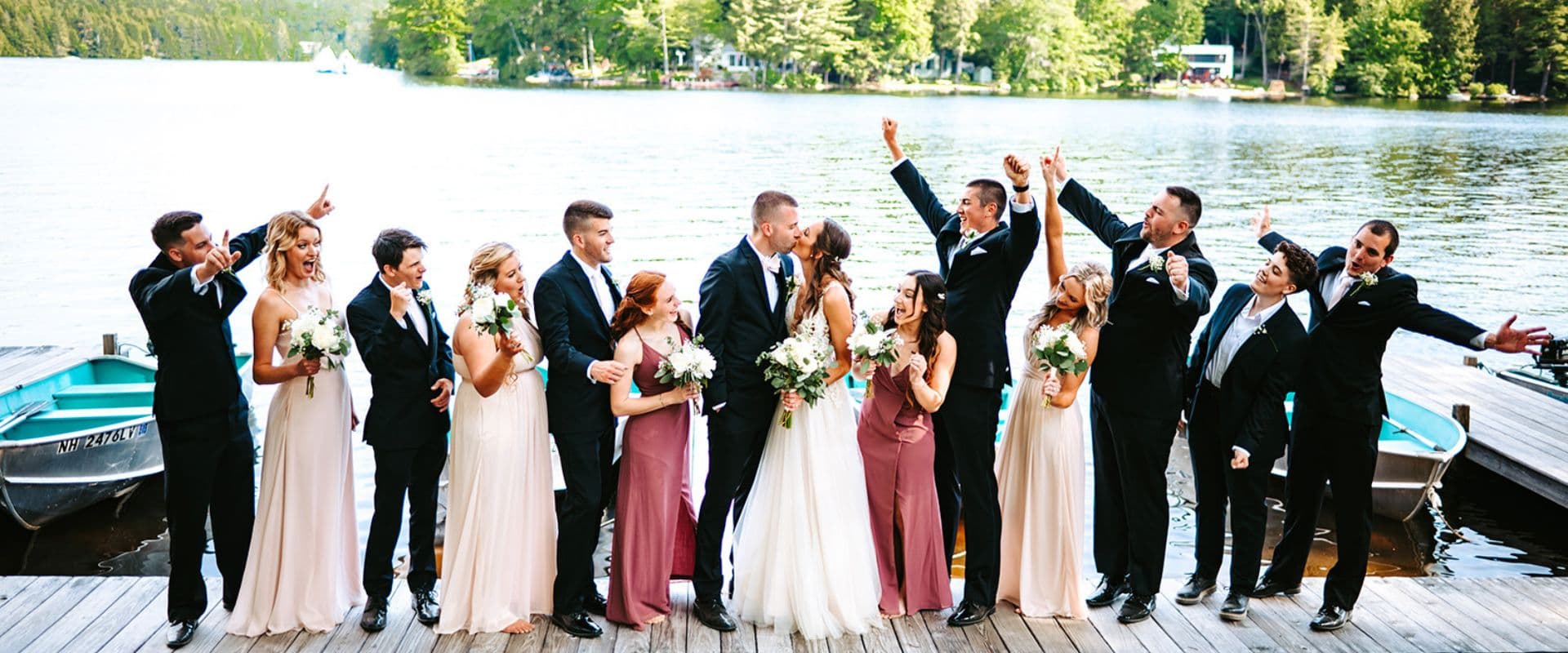 A wedding party lined up for a photo on a dock by a large lake A wedding party lined up for a photo on a dock by a large lake